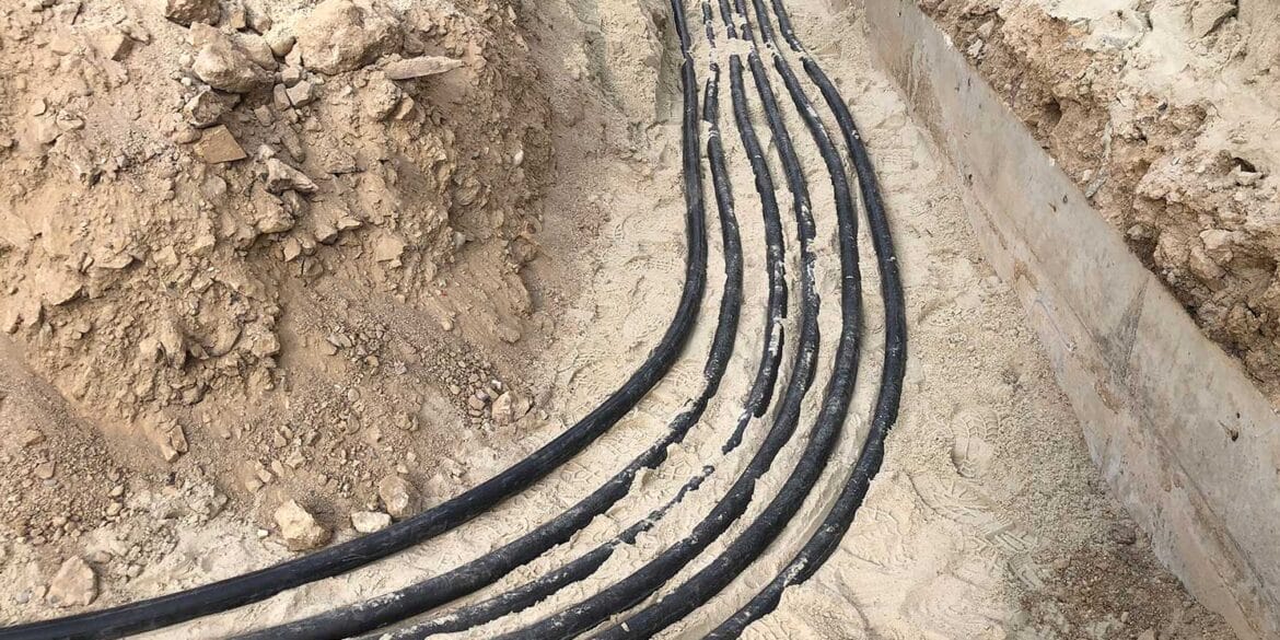 Several black cables are laid side by side in a trench filled with sand and soil, likely for underground installation or utility work.
